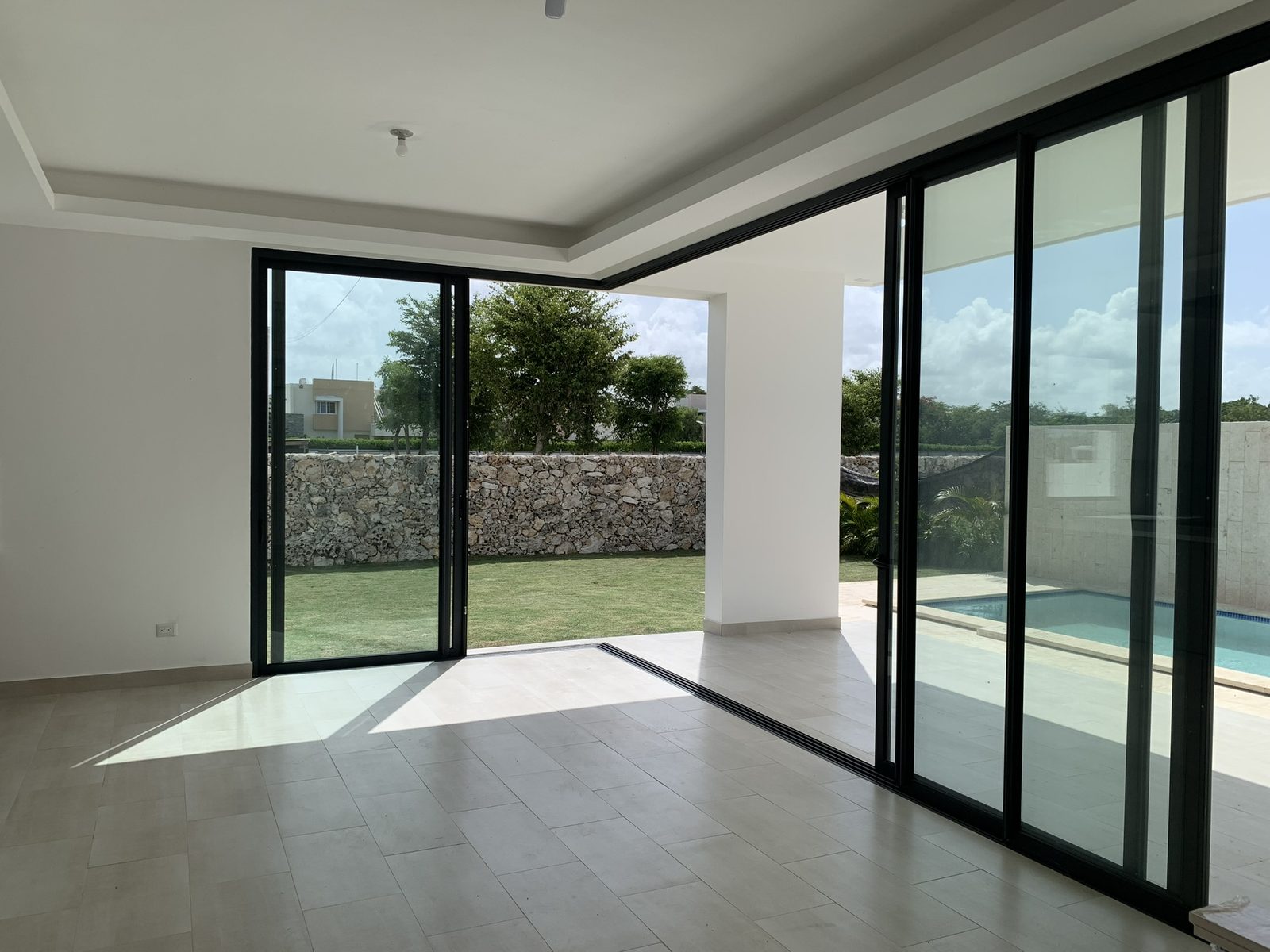Sala con ventanales corredizos al jardín y la piscina